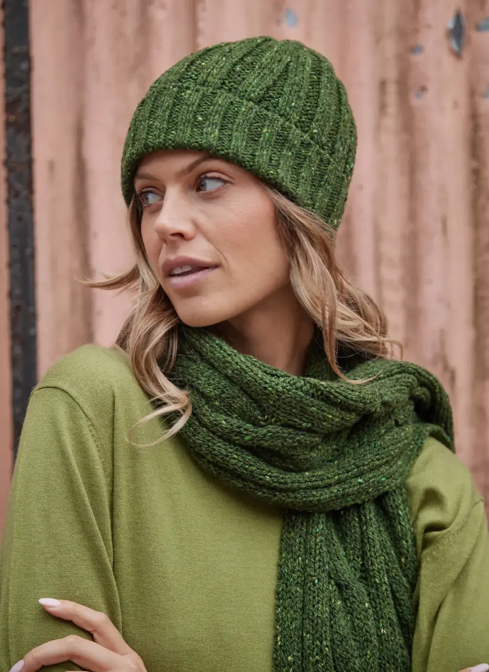 Woman wearing a ribbed Fisherman Donegal fleck beanie in shamrock green, styled with a matching cable knit scarf.